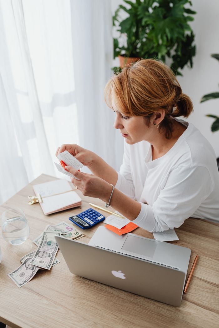 contact-img Woman calculating budget with laptop, cash, and receipts at desk.