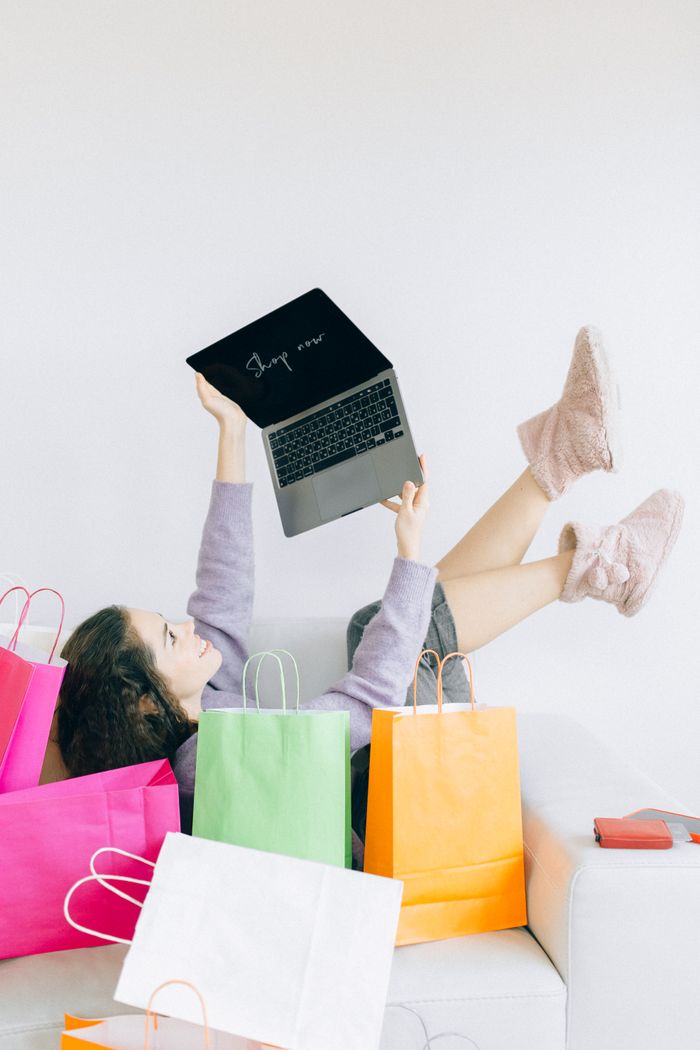 gallery-3 Woman lying on couch with laptop and colorful shopping bags, embodying online shopping joy.